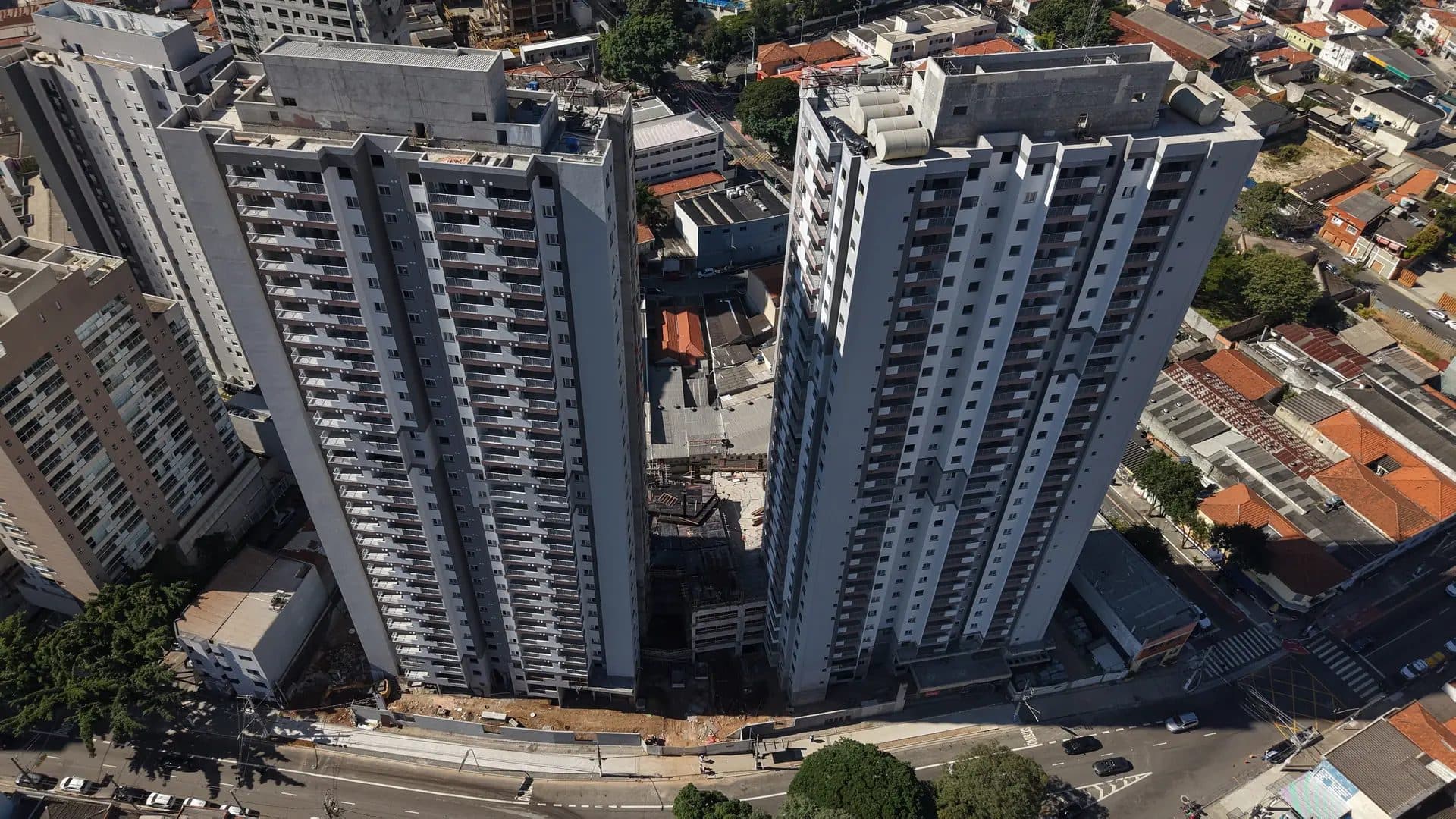 Vista aérea superior dos prédios em construção e bairro residencial no entorno.