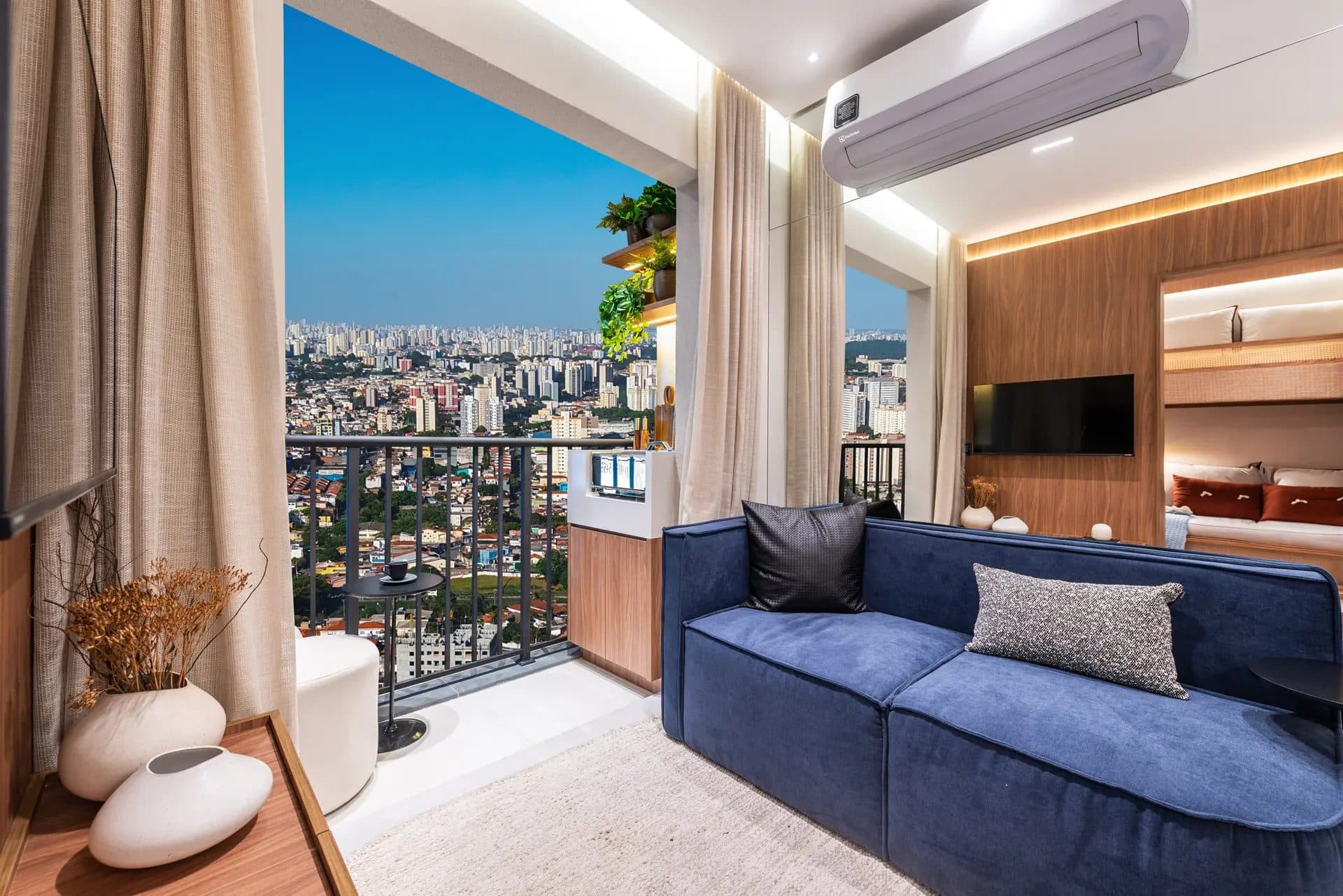 Sala integrada com varanda gourmet, sofá azul e vista panorâmica da cidade